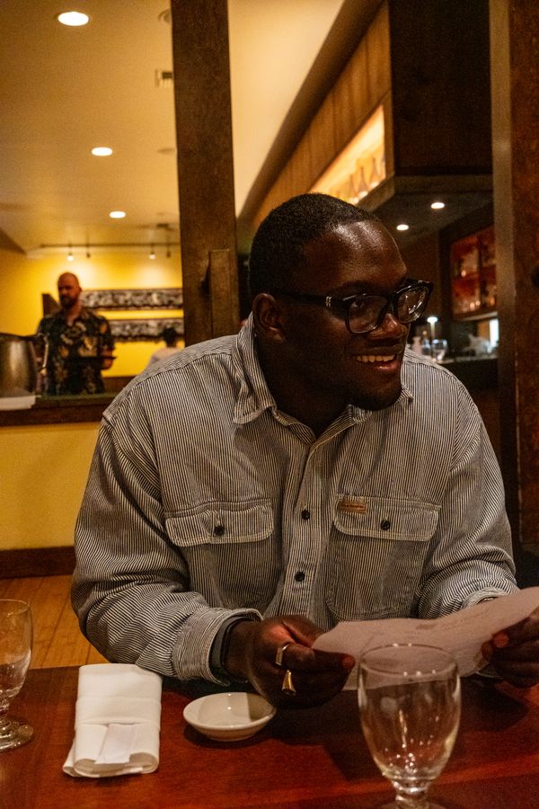 A man in glasses laughs while reading a menu at a warmly lit restaurant
