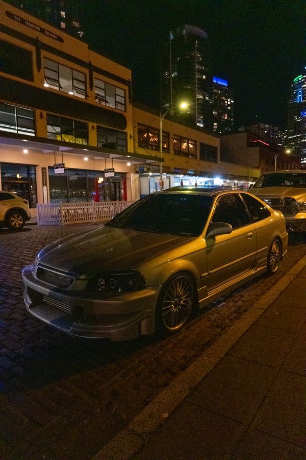 A silver sedan parked on a city street at night under neon and streetlights