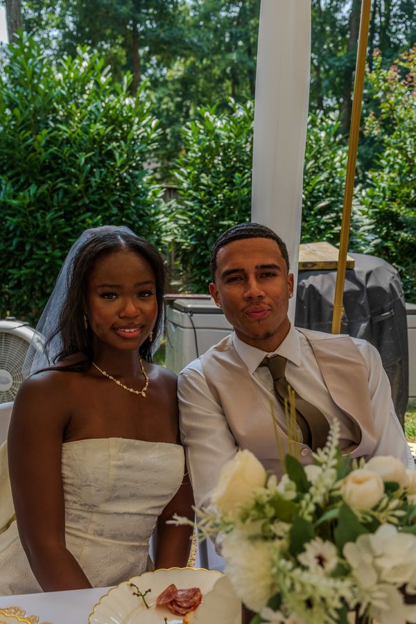 Bride and groom seated together at the reception table behind a bouquet of white flowers