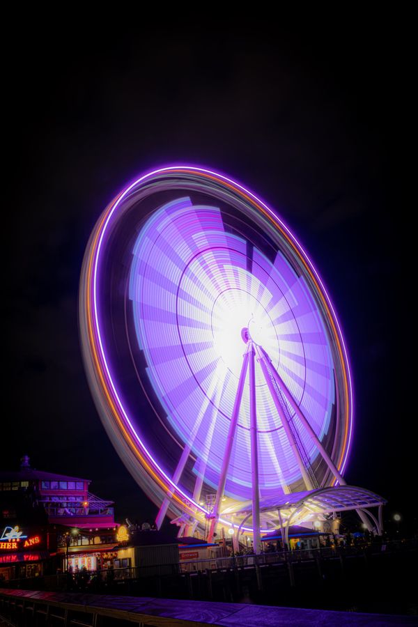 Long exposure of the Seattle Great Wheel at night, its lights blurred into purple and white rings